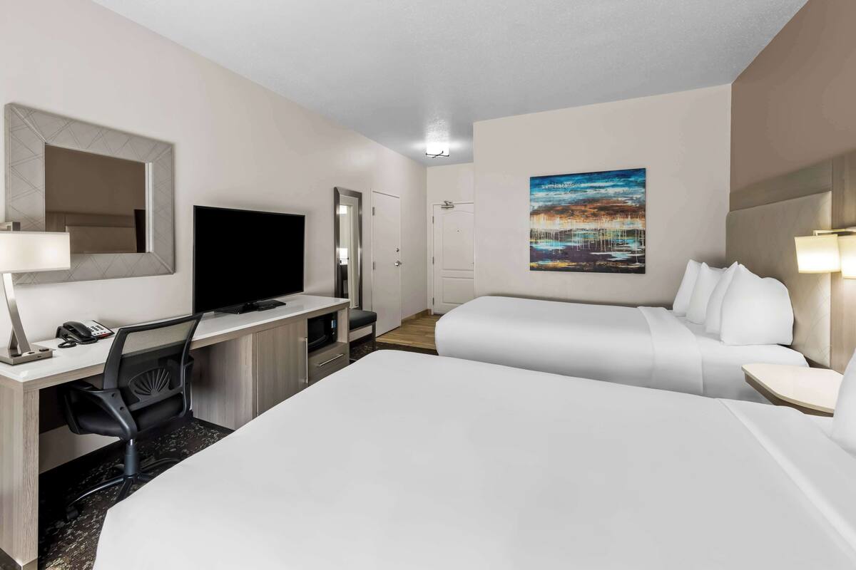 A hotel room with a bed, a desk with a computer, a chair, a TV, and a painting on the wall.