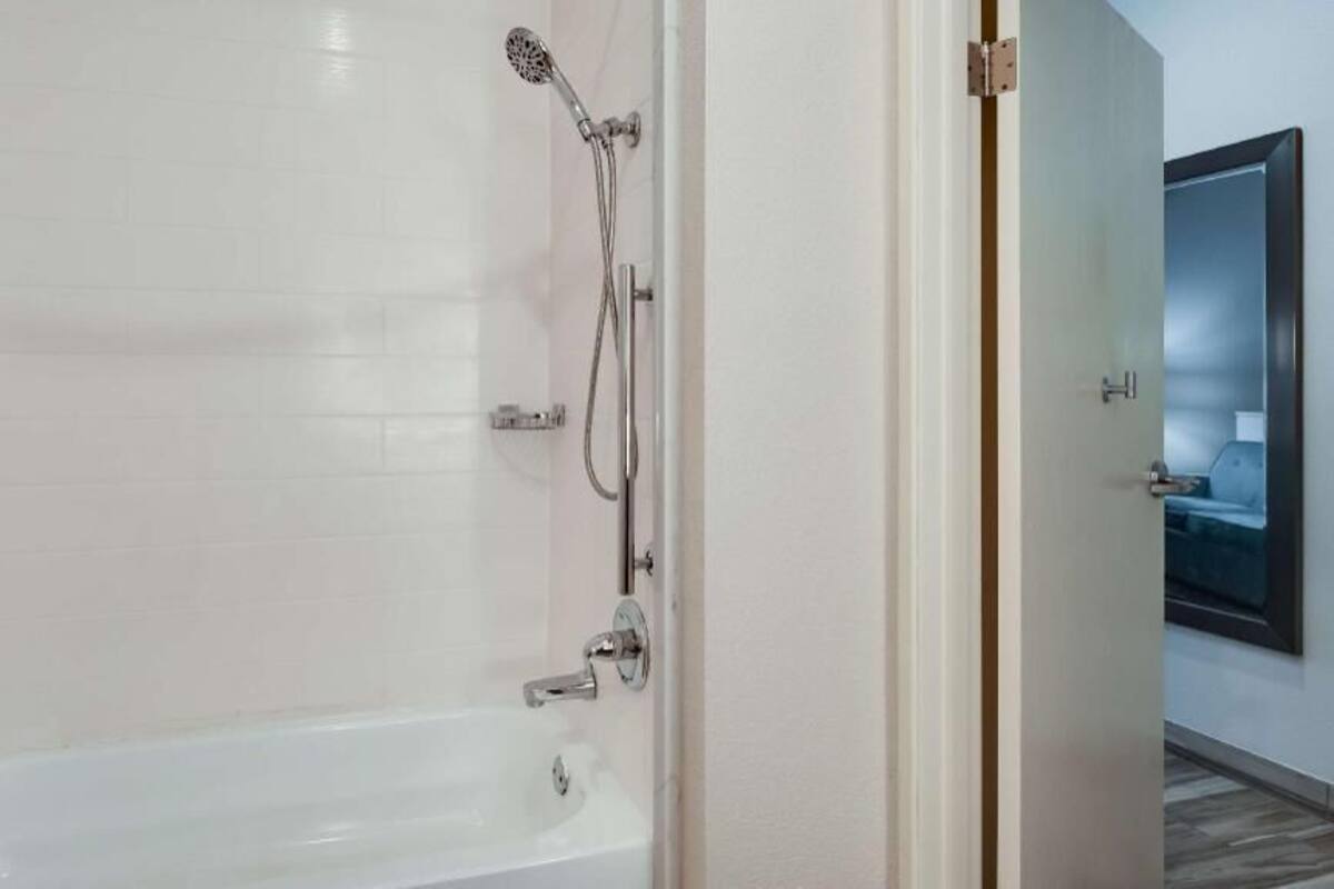 A bathroom with a shower, a bathtub, and a door leading to another room.