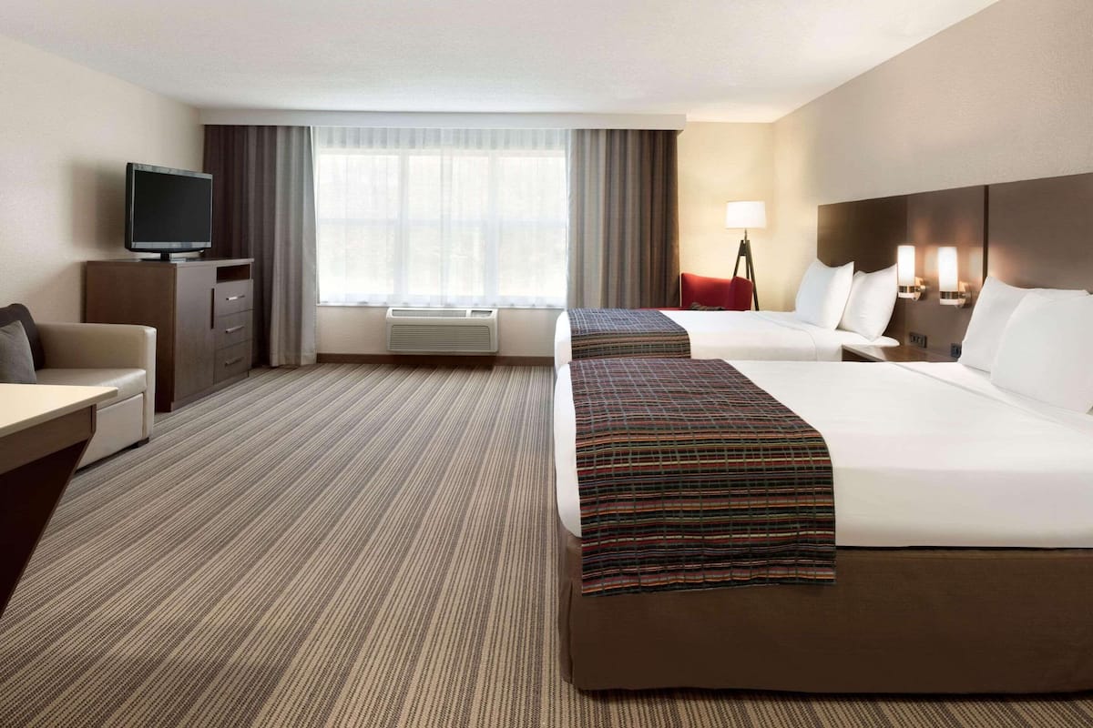 A hotel room with two beds, a desk, a television, and a window with curtains.