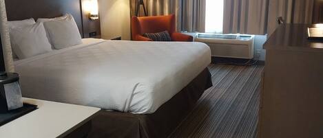 Et hotelværelse med en stor seng, et skrivebord, en stol, en lampe og et klimaanlæg.