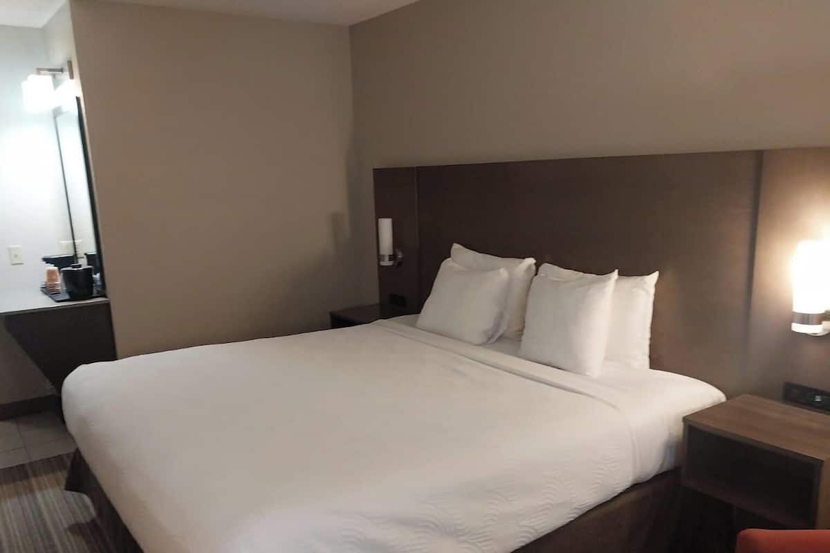 A hotel room with a large bed, a bedside table, a nightstand, a mirror, and a wall-mounted light.