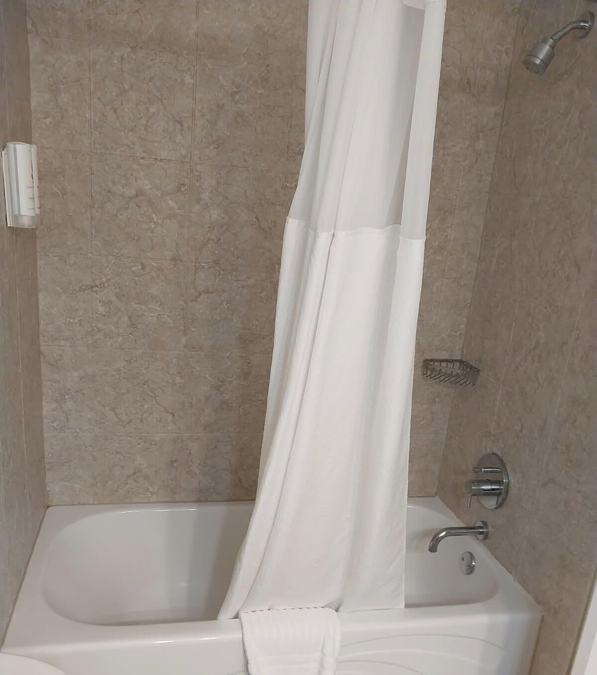 Un baño con bañera, cortina de ducha y cabezal de ducha.