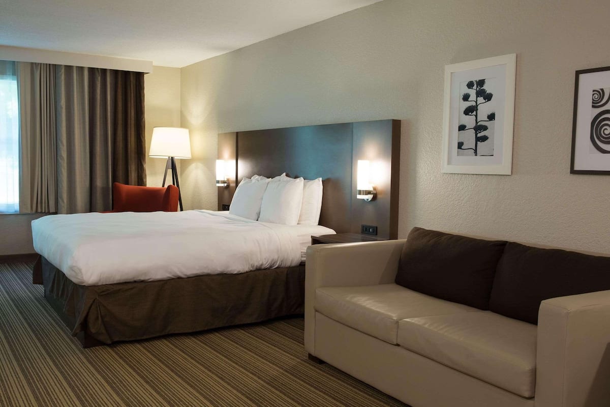 A hotel room with a large bed, a sofa, two wall-mounted lamps, and framed artwork on the wall.