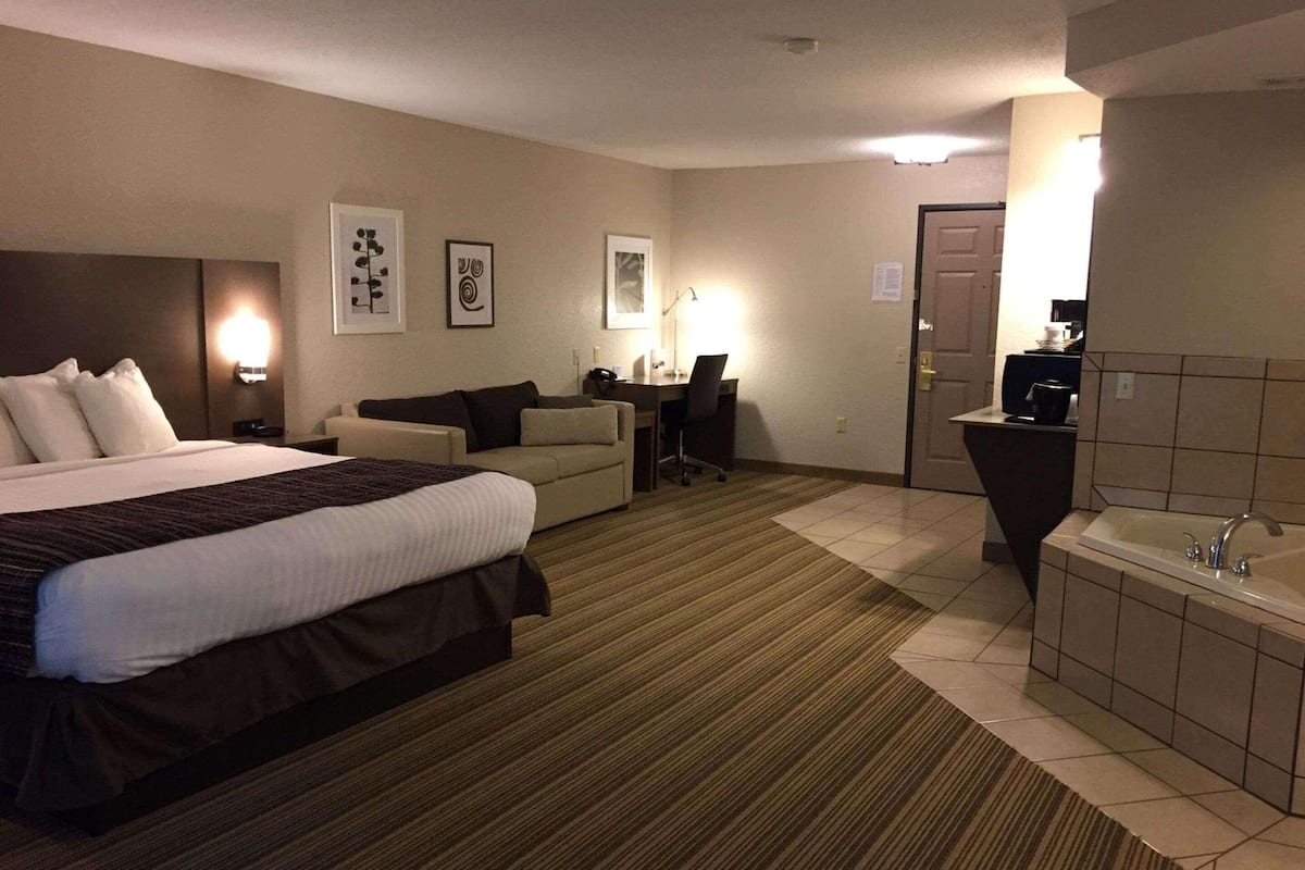 A hotel room with a large bed, a sofa, a desk, a chair, and a bathroom with a bathtub and sink.