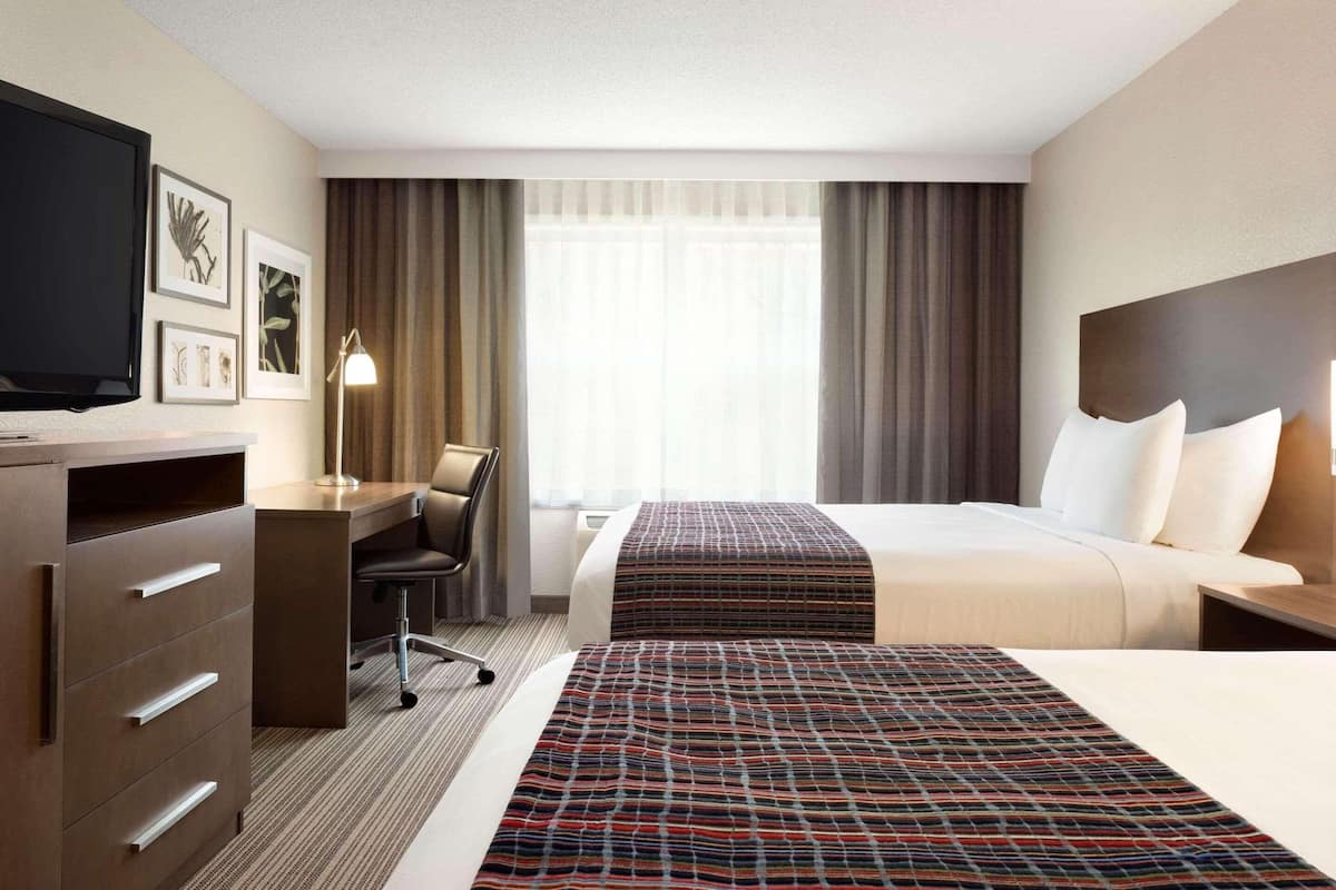 A hotel room with a bed, a desk, a chair, a television, and a window with curtains.