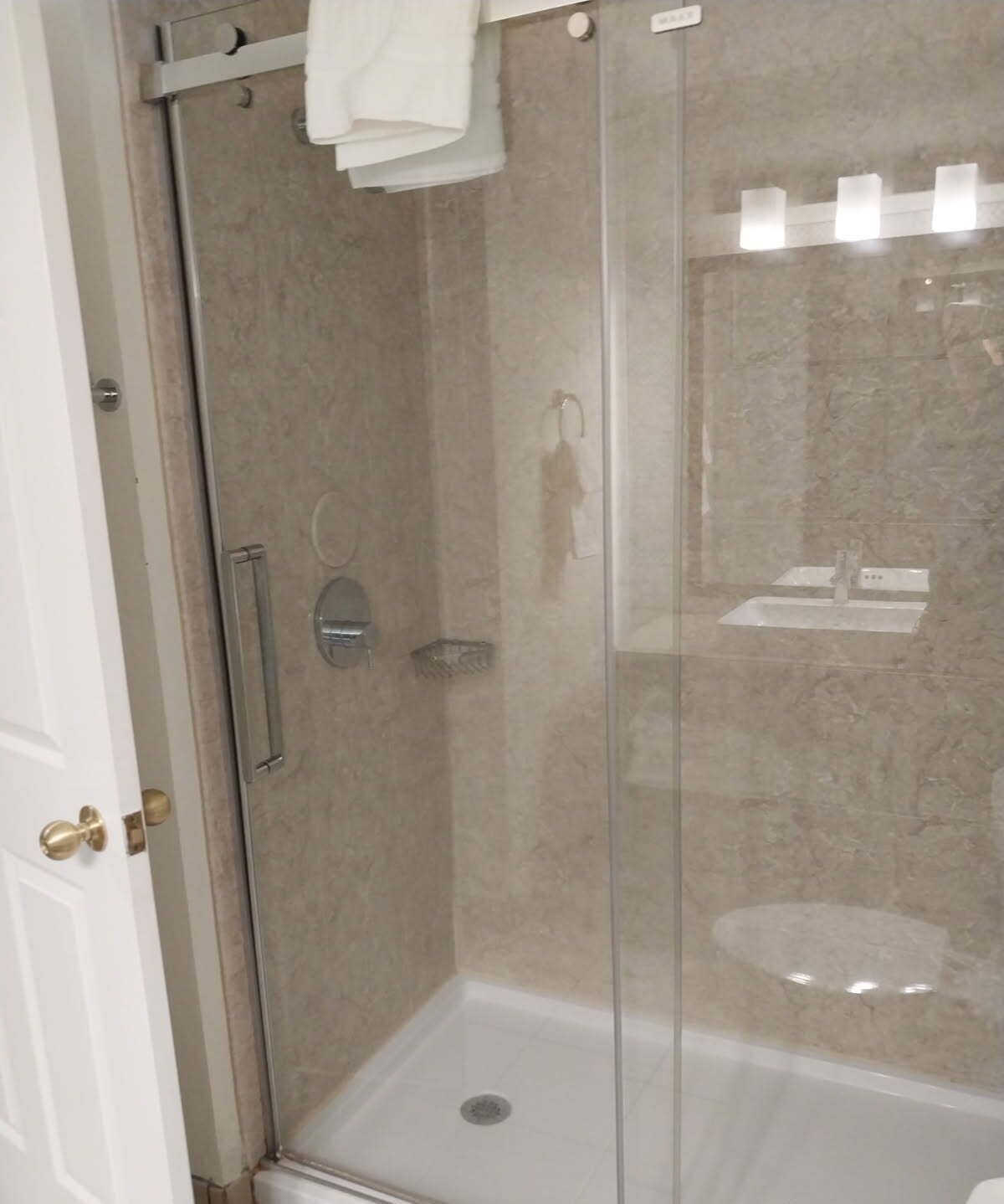 Une cabine de douche fermée par des parois en verre, avec une serviette blanche accrochée à la poignée de la porte, une porte de douche en verre et un mur recouvert de carreaux.