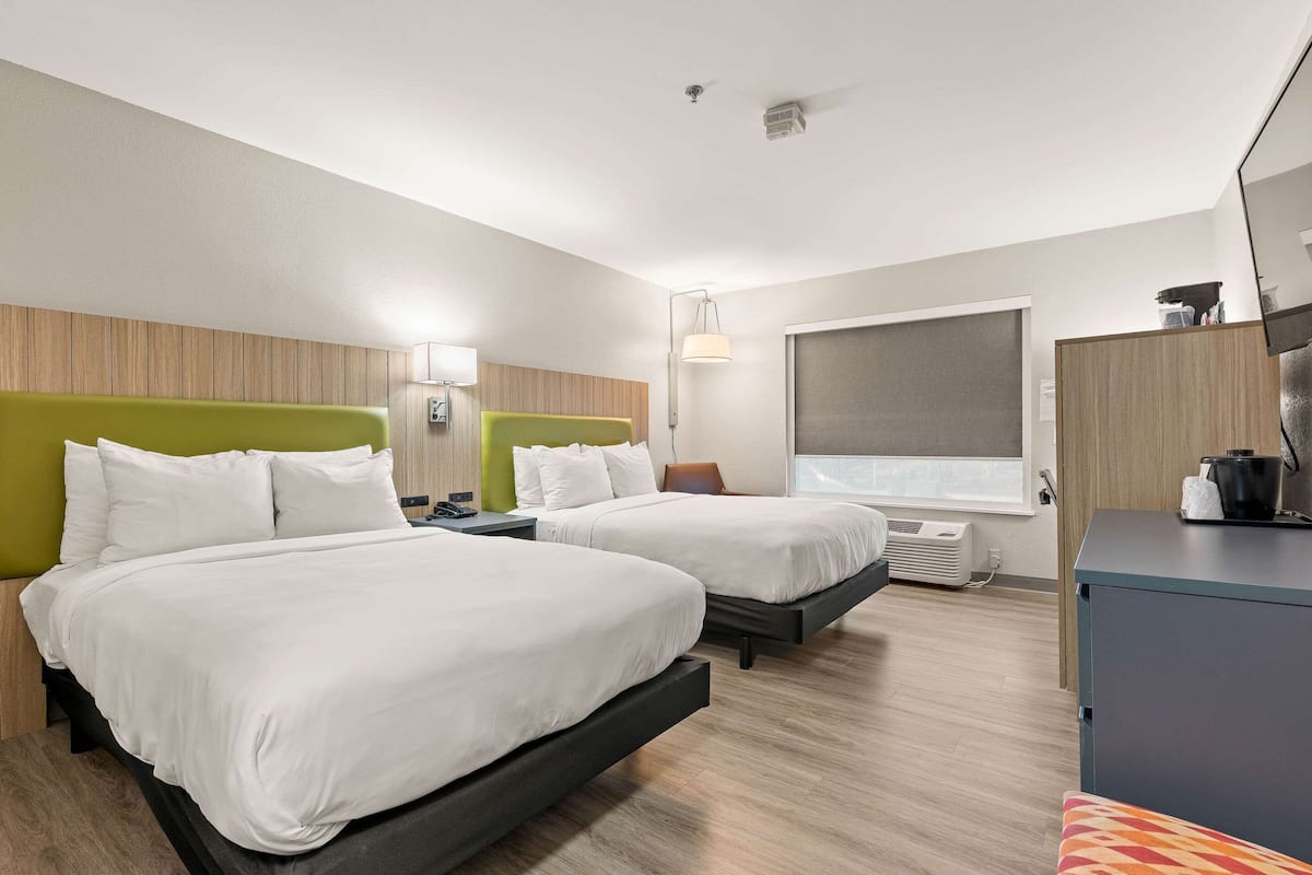 A hotel room with two beds, a desk, a chair, a window, and a kitchenette.