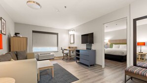Ein modernes Hotelzimmer mit einer Couch, einem Schreibtisch, einem Fernseher, einem Bett und einem durch eine offene Tür einsehbaren Badezimmer.