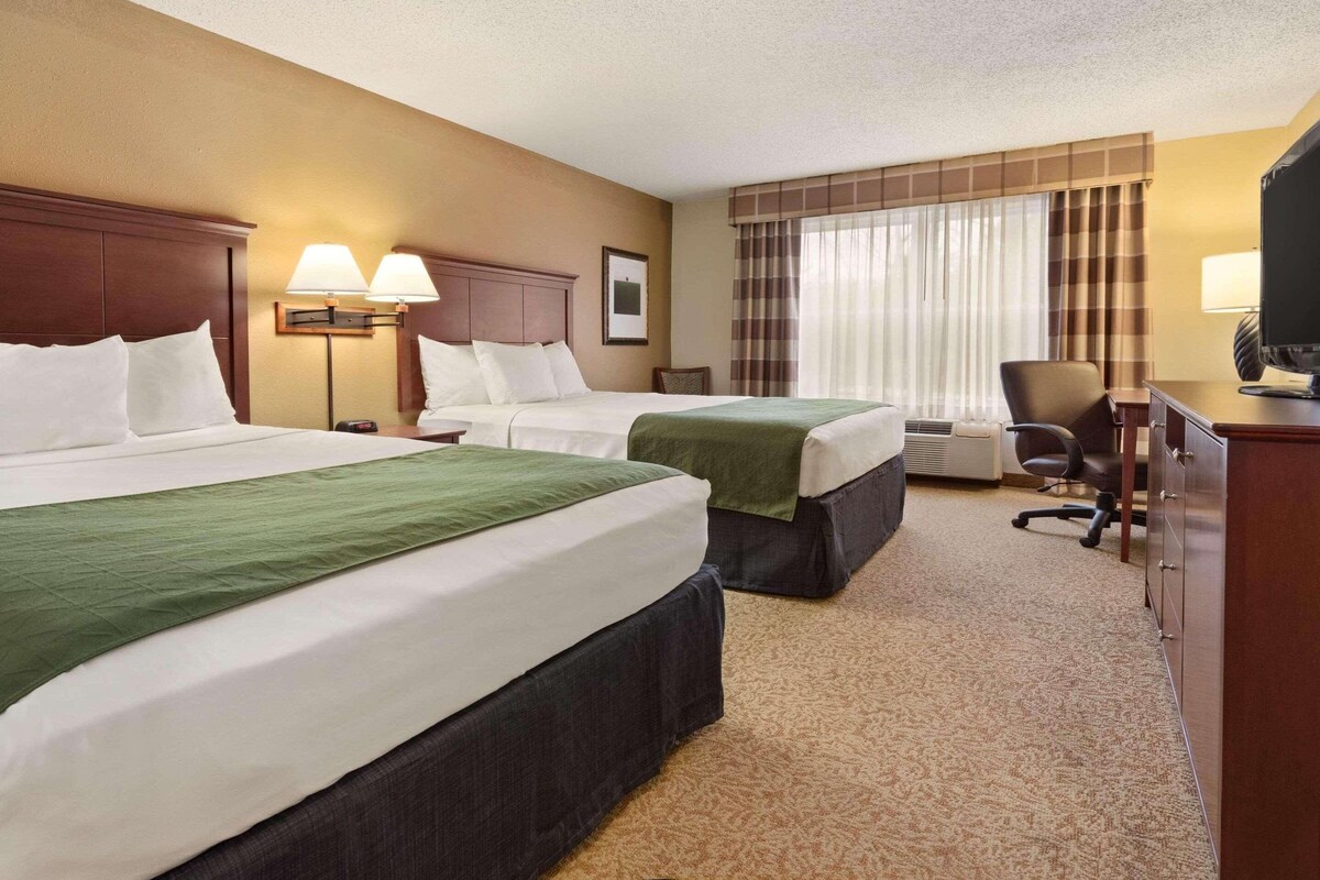 A hotel room with two beds, a desk, a chair, and a television.