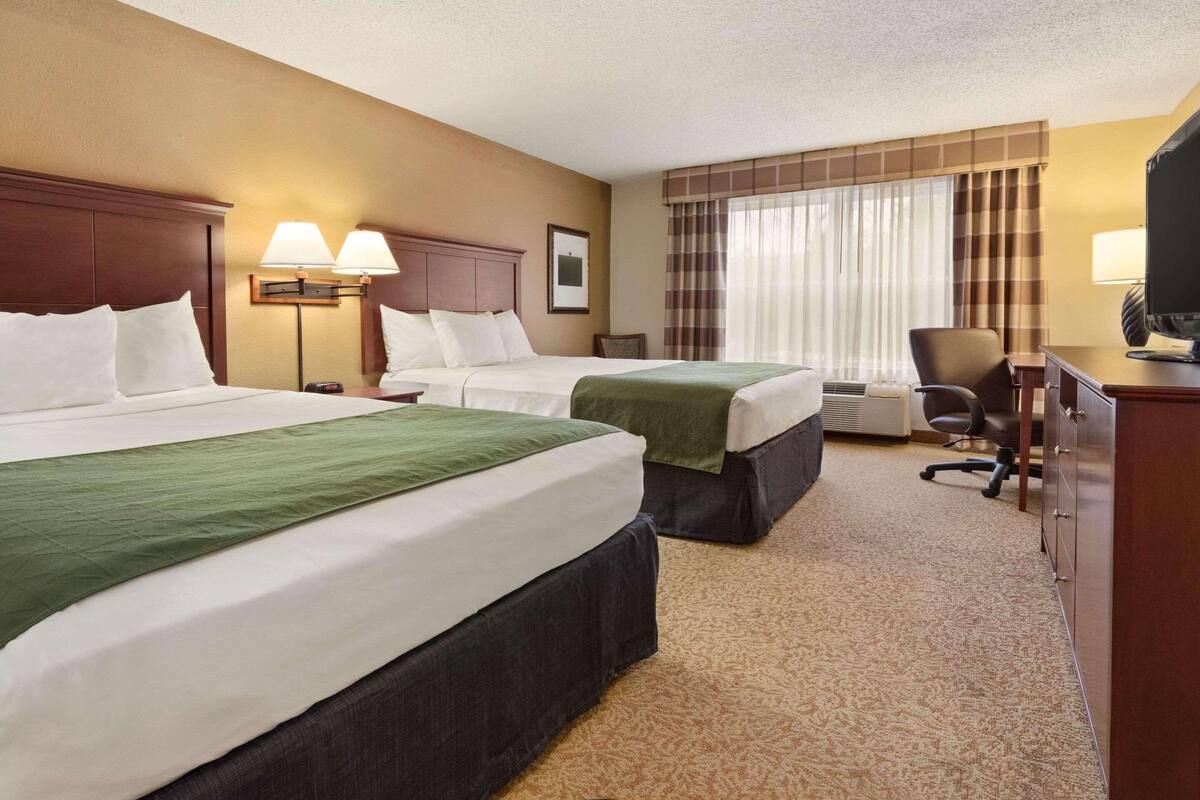 A hotel room with two beds, a desk, a chair, and a television.