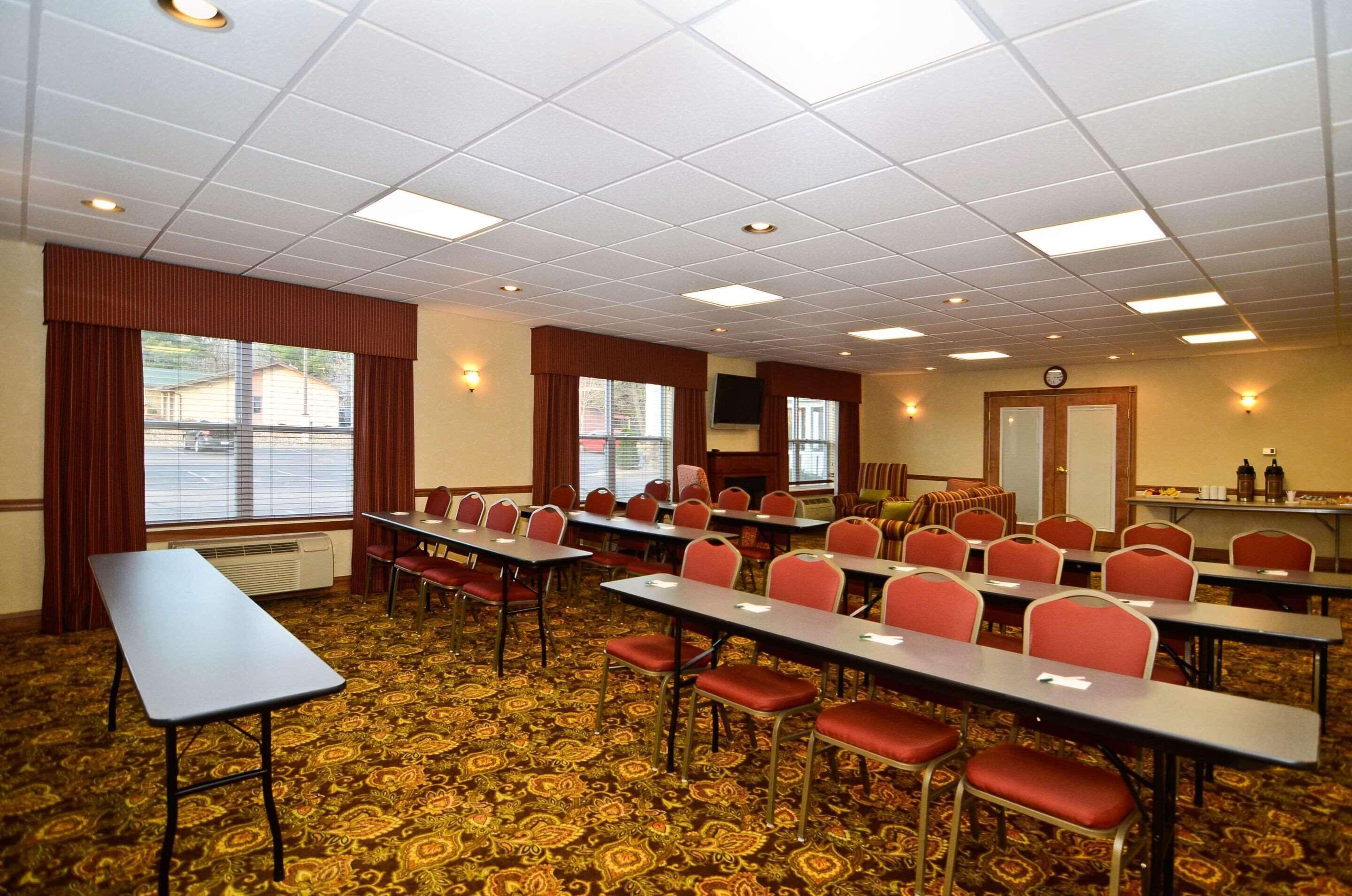 A conference room with multiple tables and chairs, a patterned carpet, and a large window with curtains.