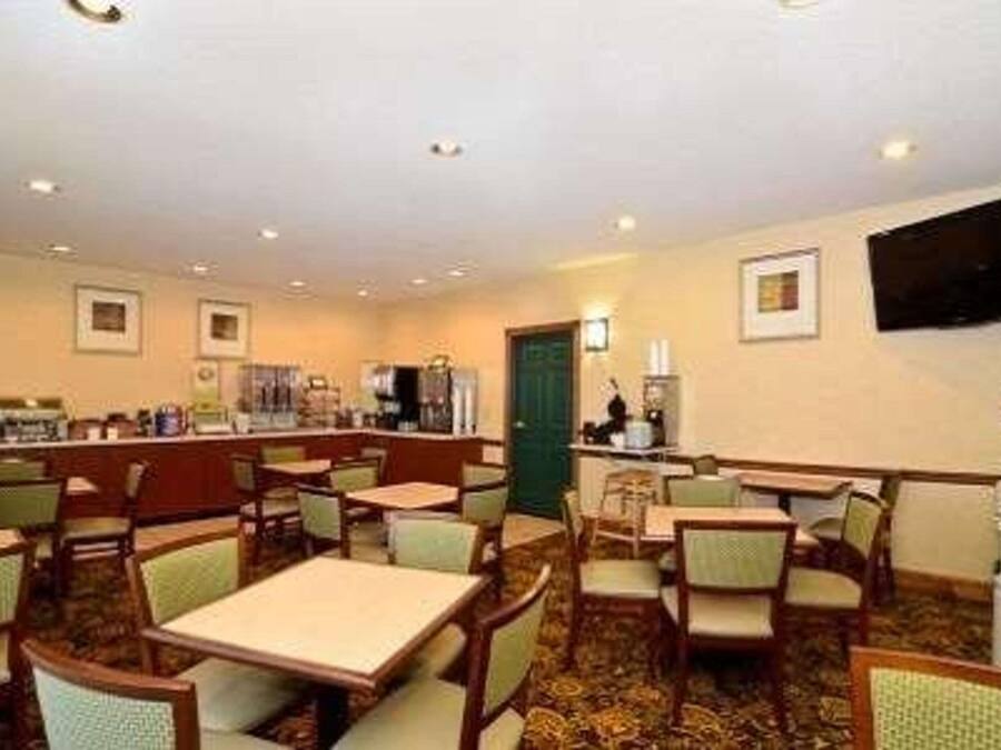 Een restaurantgedeelte in een hotel met meerdere tafels en stoelen, een balie met een kassa en een flatscreen televisie aan de muur.