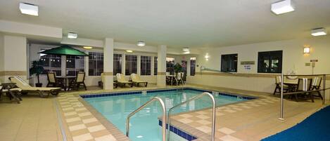 An indoor swimming pool with tiled flooring, lounge chairs, and a no diving sign.