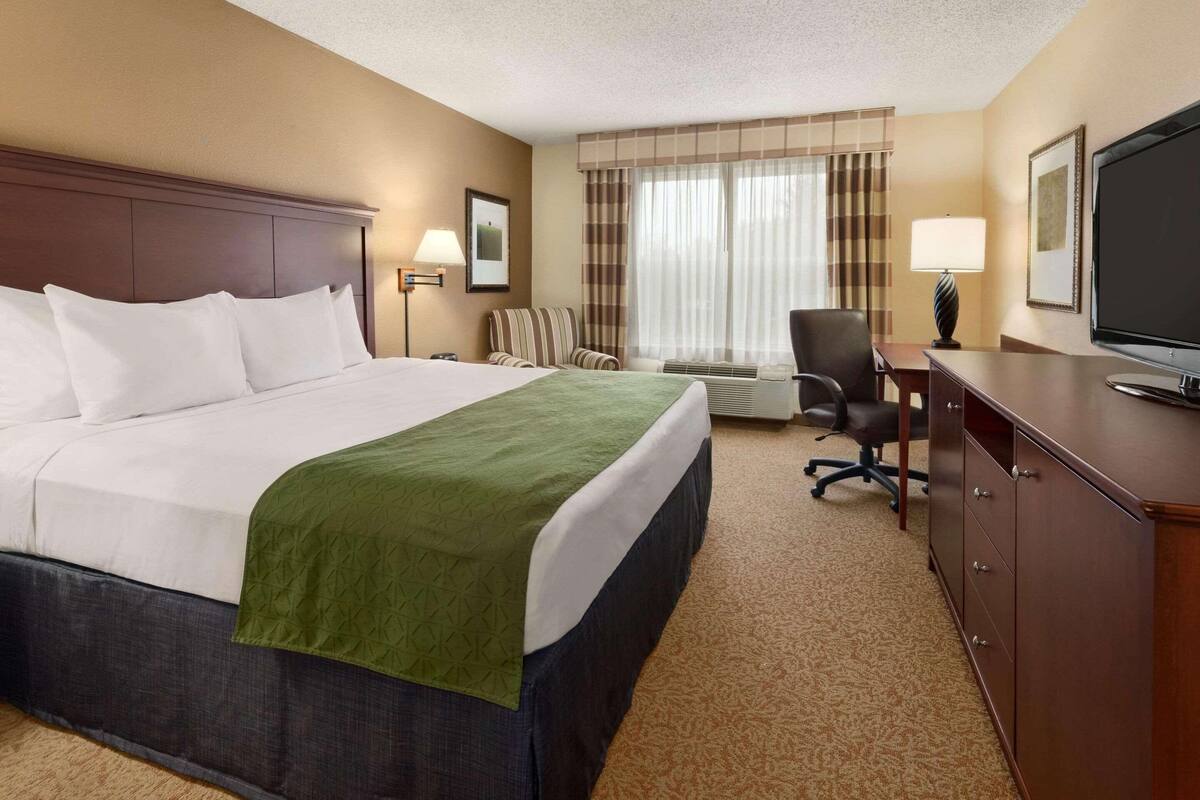 A hotel room with a large bed, a desk, a chair, a television, and a window with curtains.