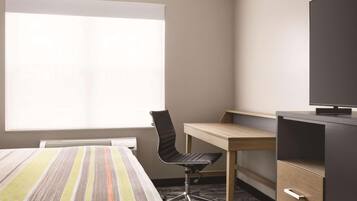A hotel room with a large bed, a desk with a chair, a television, and a window with blinds.