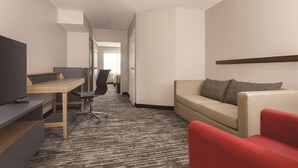 Une chambre d’hôtel équipée d’un bureau, d’une télévision, d’un canapé et d’un fauteuil rouge.