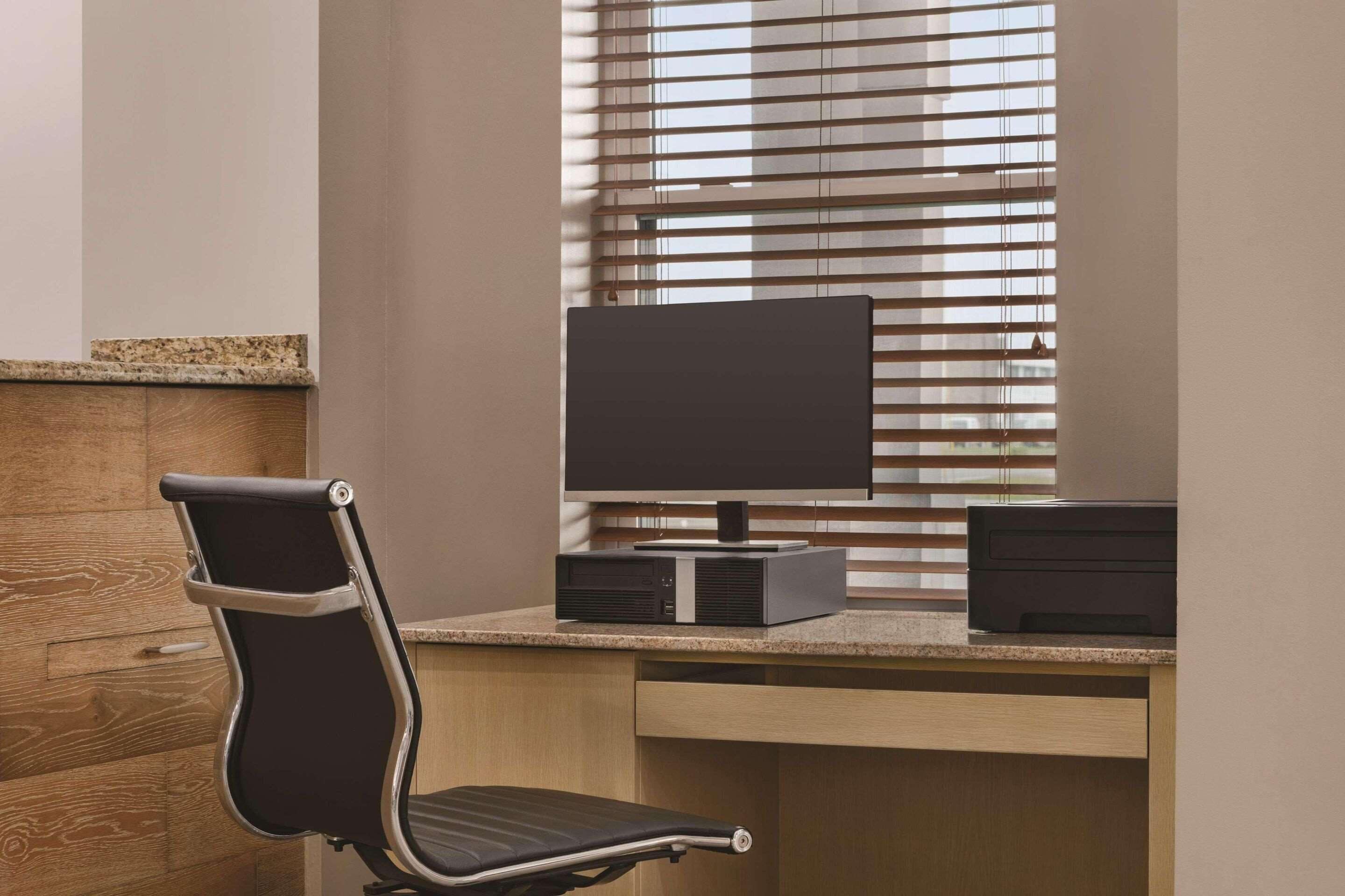 Un escritorio moderno con una computadora, una silla y una ventana con persianas.
