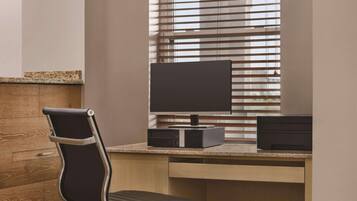 A modern office desk with a computer, a chair, and a window with blinds.
