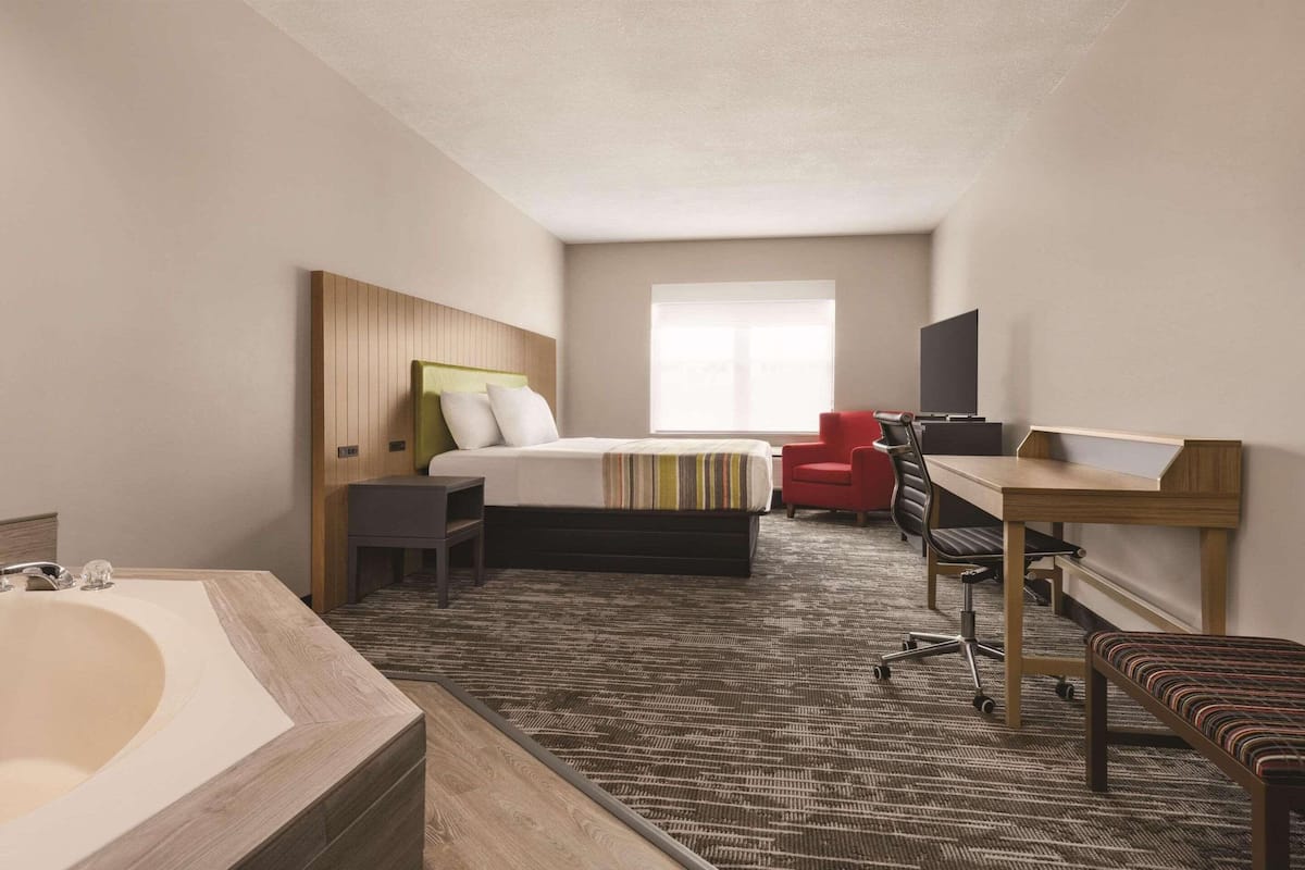 Une chambre d’hôtel avec un grand lit, un bureau, une chaise, une petite table, un banc, une télévision et une fenêtre.