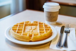 A plate with a waffle and a cup of coffee on a table.