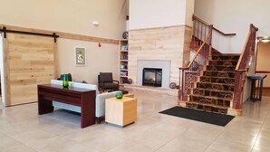 A spacious lobby with a reception desk, seating area, fireplace, and a staircase with ornate railings. - Country Inn & Suites by Radisson, Milwaukee West (Brookfield), WI (Brookfield)