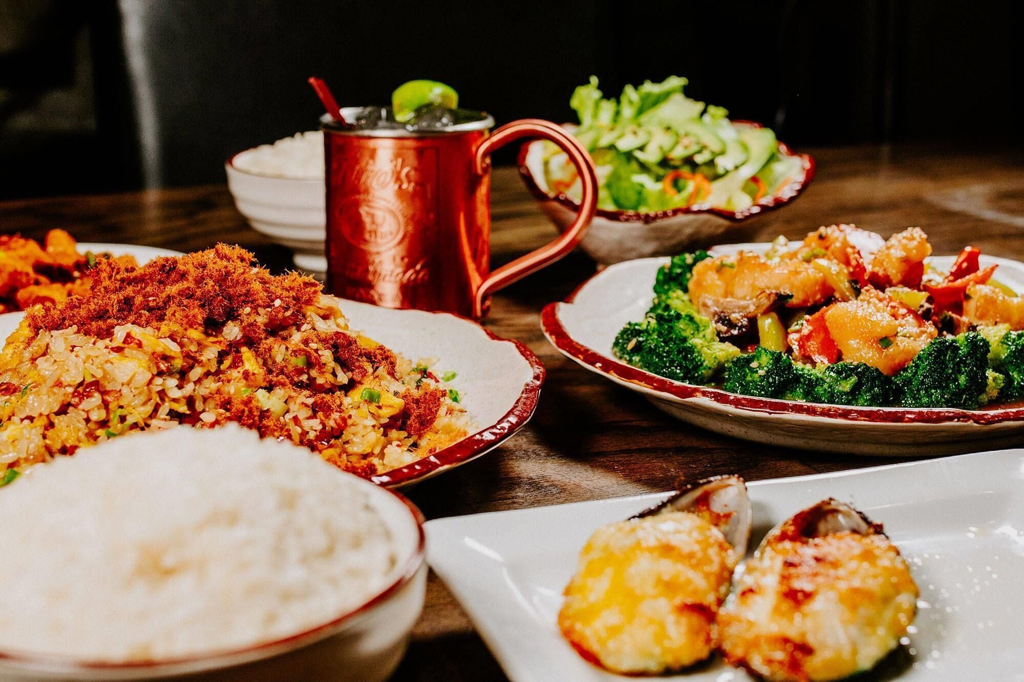 A table with various dishes including fried rice, broccoli, and seafood, along with a red mug and a white bowl.