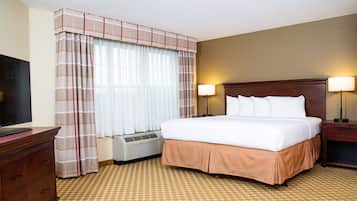 A hotel room with a large bed, two bedside lamps, a TV, a dresser, and a window with curtains.