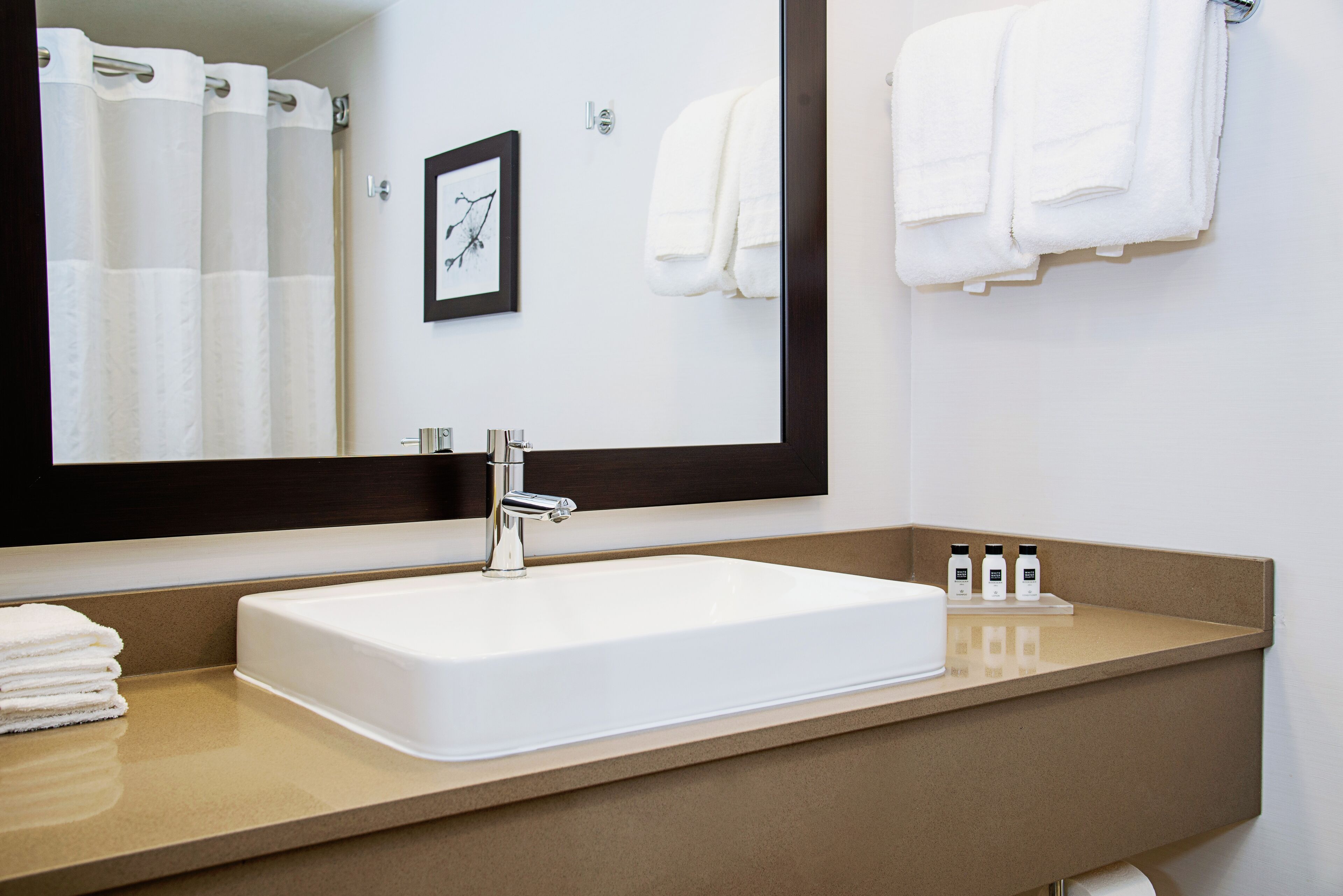 A bathroom with a white sink, a large mirror, and a towel rack with folded towels.
