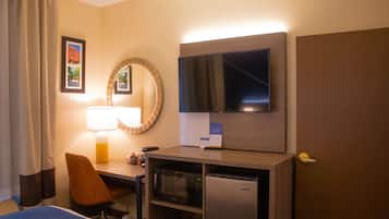 Habitación de hotel con una cama, un escritorio con lámpara, microondas, refrigerador, televisión y una puerta.