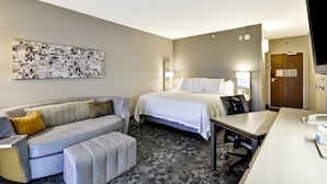 A hotel room with a bed, a sofa, a desk, and a large abstract painting on the wall.