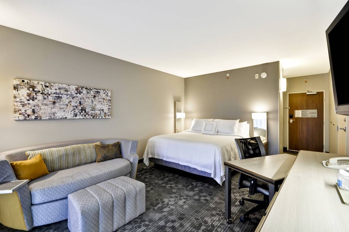 A hotel room with a bed, a sofa, a desk, and a large abstract painting on the wall.