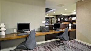 A reception desk with two computer monitors, a printer, and a keyboard. There are two chairs in front of the desk. The room has a carpeted floor and a wooden desk.