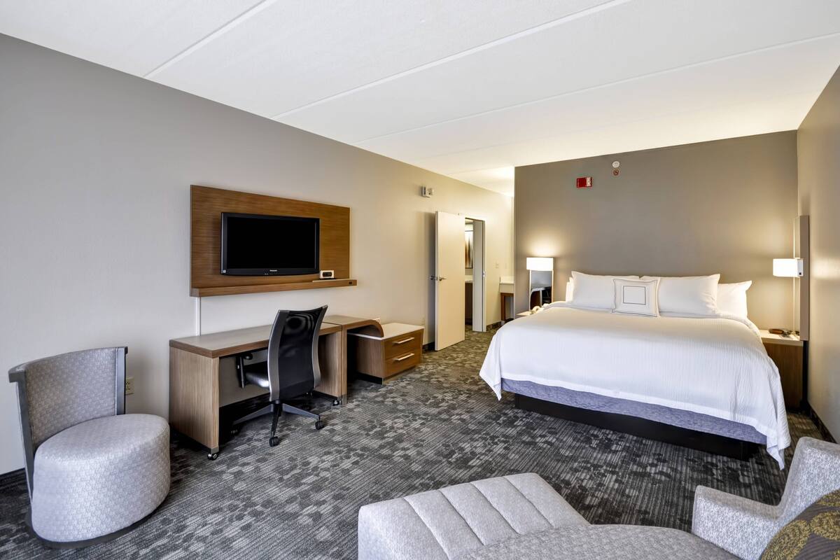 A hotel room with a bed, desk, chair, and television.