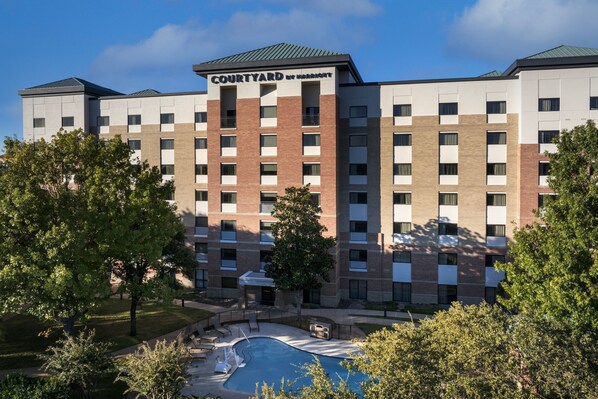 A Courtyard by Marriott hotel with a swimming pool, surrounded by trees and greenery.