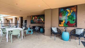 An outdoor patio area with seating arrangements, including tables and chairs, and two large paintings on the walls.