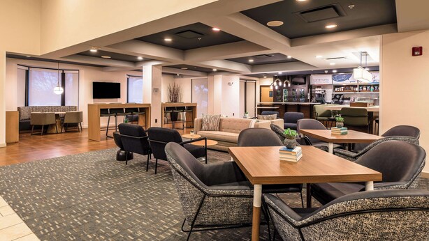 A modern lounge area with a wooden table, comfortable seating, and a bar in the background. - Sonesta Select Dallas Richardson (Richardson)