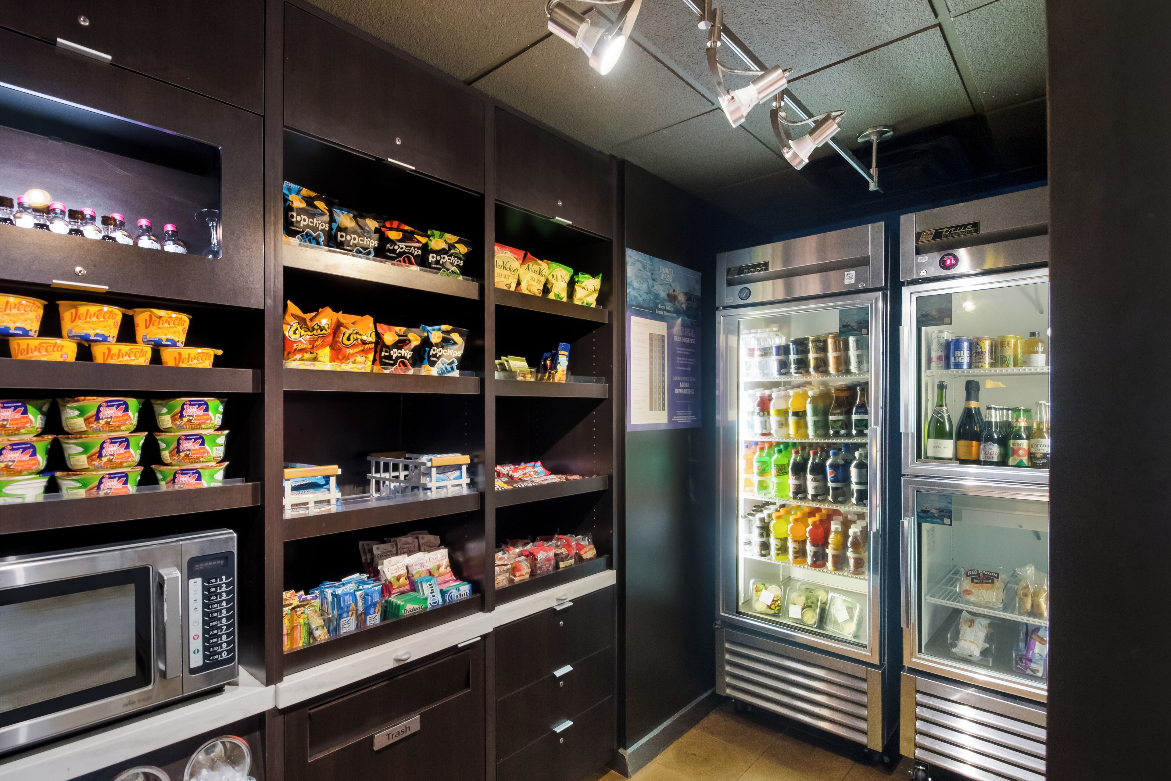 A self-service snack and beverage station with microwaves, refrigerators, and shelves stocked with snacks and drinks.