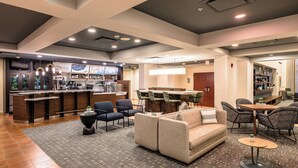 A modern hotel lobby with a bar area, seating arrangements, and a reception desk.