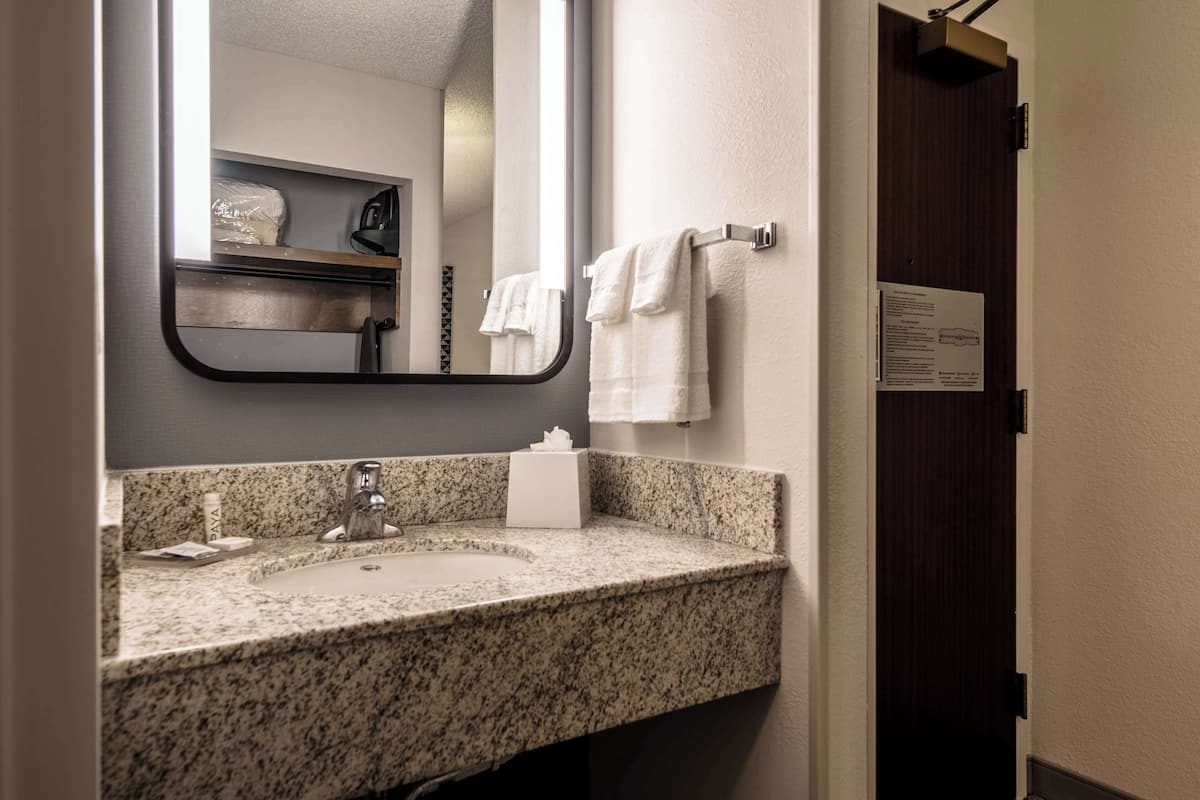 A bathroom with a granite countertop sink, a mirror, and a towel rack.