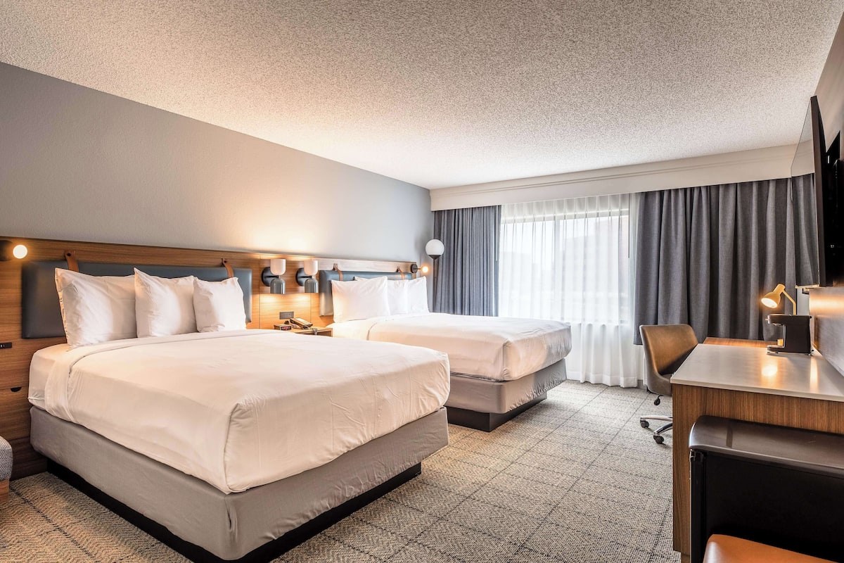 A hotel room with two beds, a desk, and a chair.