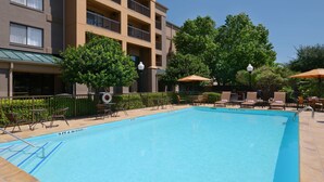 A swimming pool with lounge chairs and umbrellas, surrounded by a building with balconies and trees.
