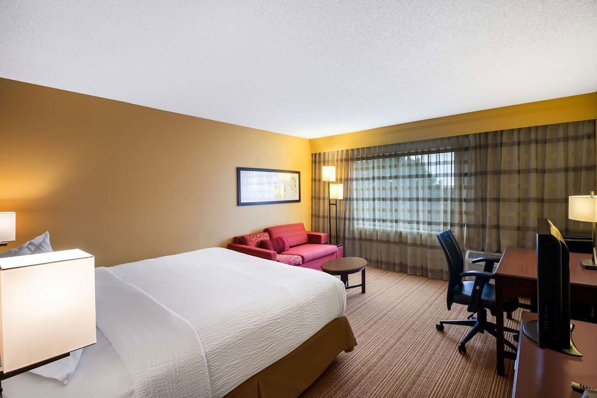 A hotel room with a bed, a desk, a chair, a sofa, and a lamp.