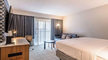 A hotel room with a large bed, a desk with a lamp, a chair, a small table, and a sofa.