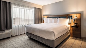 A hotel room with a large bed, a bedside table with a lamp, and a window with curtains. - Sonesta Select Dallas Richardson (Richardson)