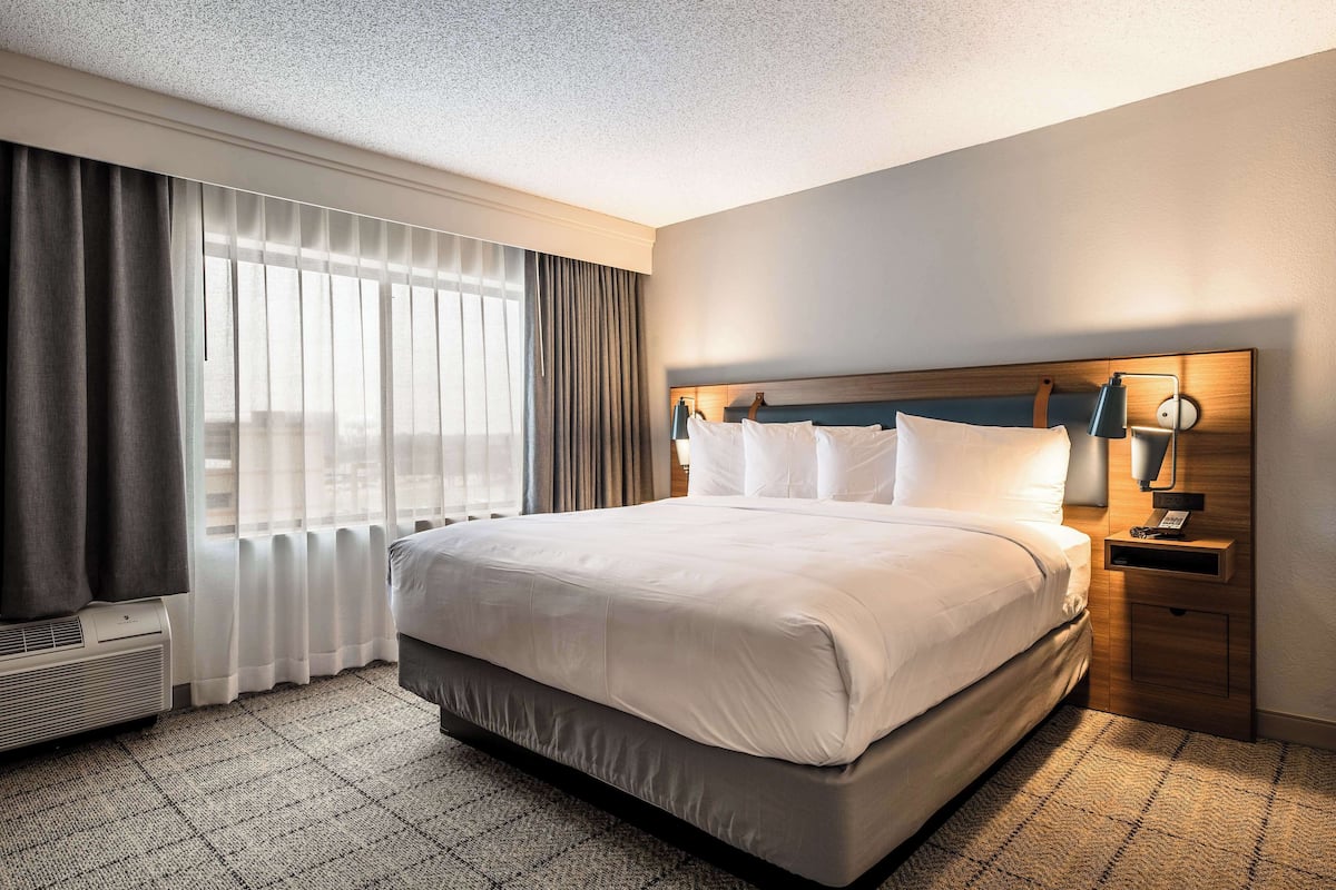 A hotel room with a large bed, a bedside table with a lamp, and a window with curtains.