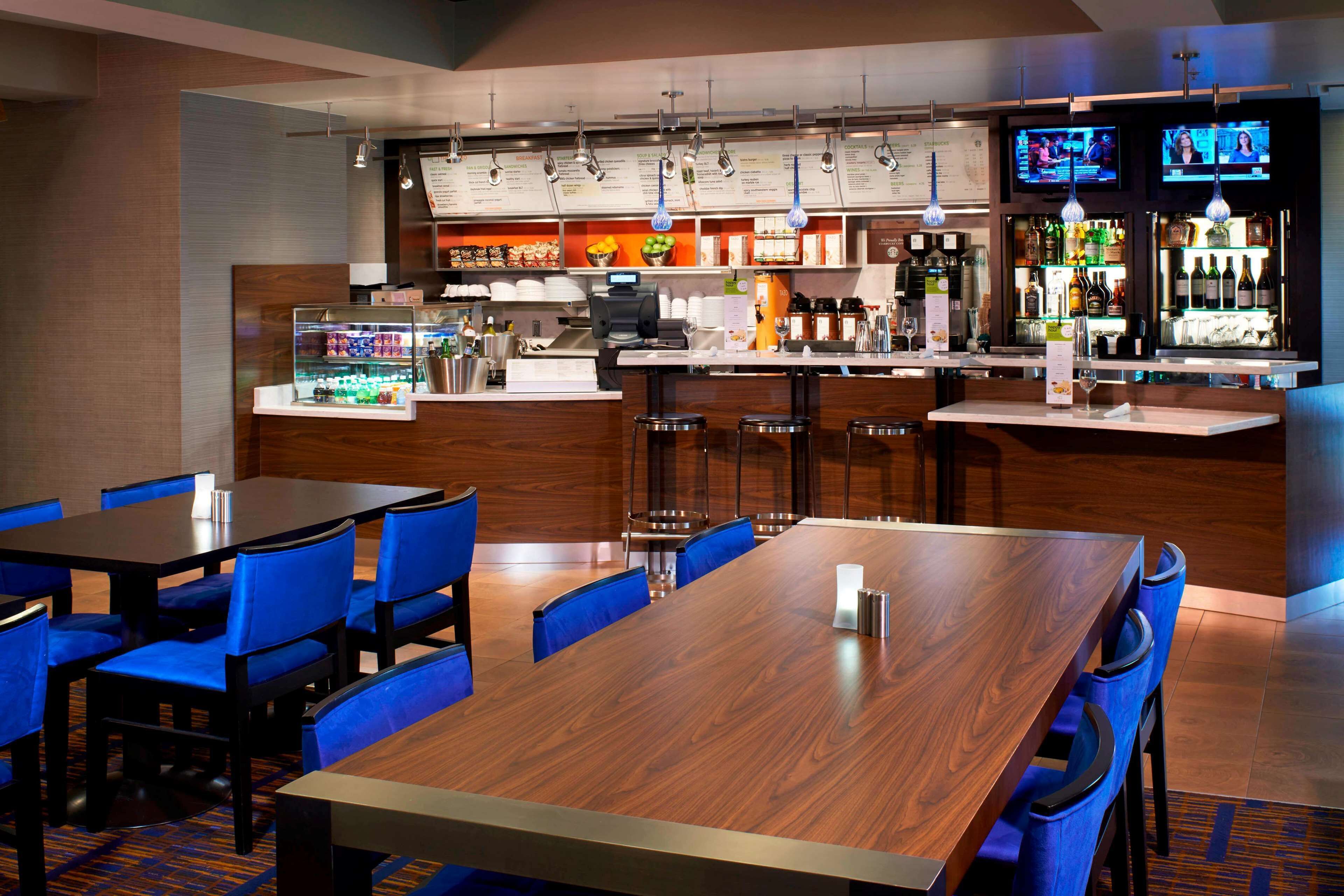 Un restaurante con zona de bar, diversas opciones de asientos como mesas y cabinas, y una variedad de alimentos y bebidas a la vista.