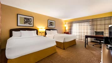 A hotel room with two beds, a desk, a chair, and a television.