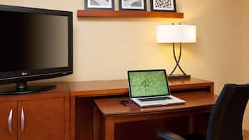 A hotel room with a wooden desk, a laptop, a flat-screen TV, a lamp, and a chair.