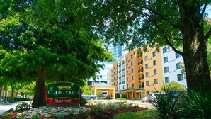 Señal de Courtyard Marriott con un jardín ajardinado, un paseo techado y un edificio de varios pisos al fondo.