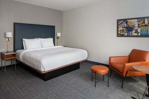 Habitación de hotel con una cama grande, una silla, una mesita y un cuadro en la pared.